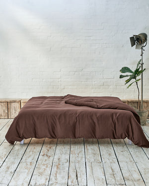 lifestyle image of acorn duvet, situated in a modern bedroom with rustic wood flooring and white exposed brick walls. 