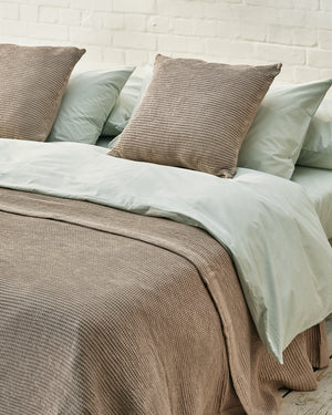 close up of beige scatter cushions and matching waffle throw on a sage green bed. 