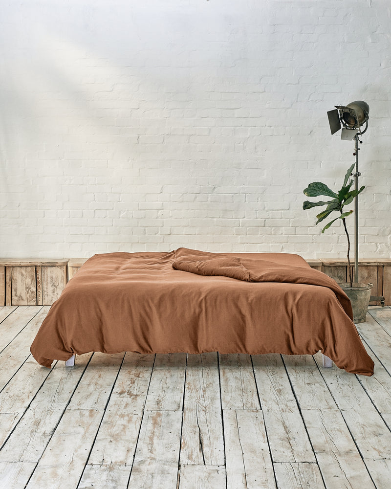 lifestyle shot of caramel brown bedding in a modern bedroom with rustic wood flooring and white walls