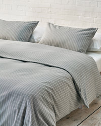 Light grey striped bedding against a white brick wall. 