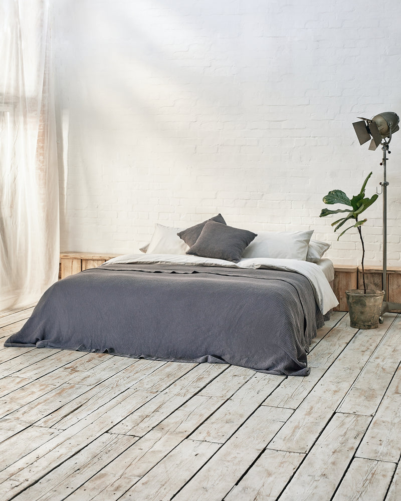 light grey bedding set with dark grey waffle bedspread and scatter cushions in an industrial bedroom