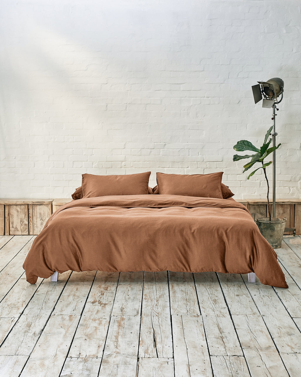 lifestyle image of caramel brown bedding in a modern bedroom with rustic wood floors and white walls.