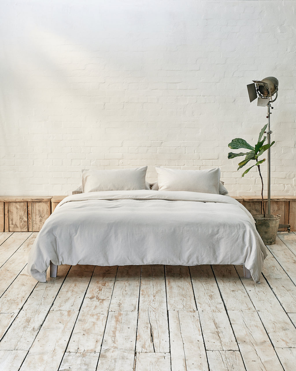 lifestyle image of cloud grey bedding, set in a modern bedroom with rustic wooden floor and white brick walls. 