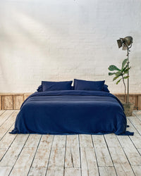 front facing lifestyle image of a navy blue bedspread on a dark blue bed. 