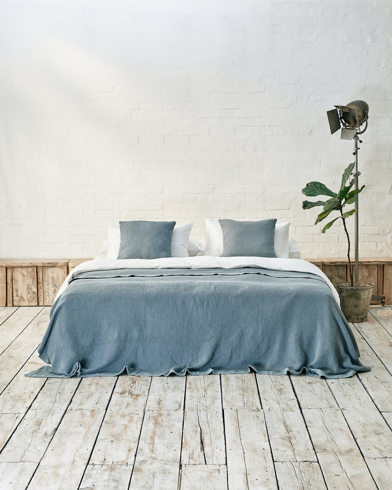 white bedding set with blue waffle bedspread and scatter cushions in an industrial bedroom