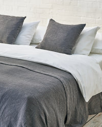 close up of dark grey waffle throw and matching cushions on a light grey bed. 