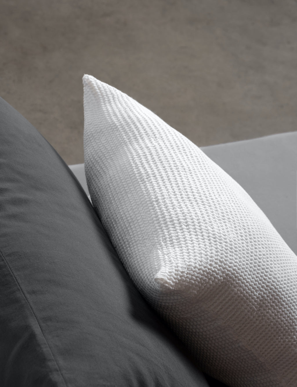 close up of white scatter cushion on a dark grey bed. 